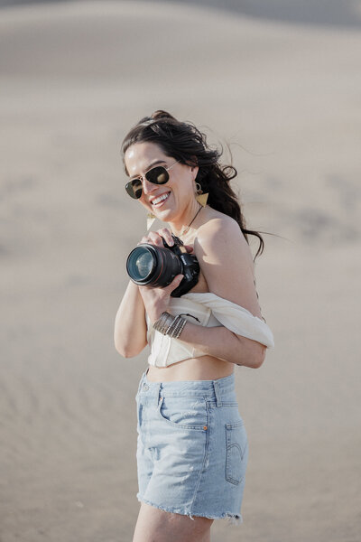 Colorado elopement photographer poses with her camera at the great sand dunes.