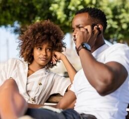A woman appears annoyed with her partner as he talks on the phone. This could symbolize a lack of communication between a couple. We offer communication therapy for couples in Florida. Contact Idit Sharoni for couples therapy exercises for communication today.