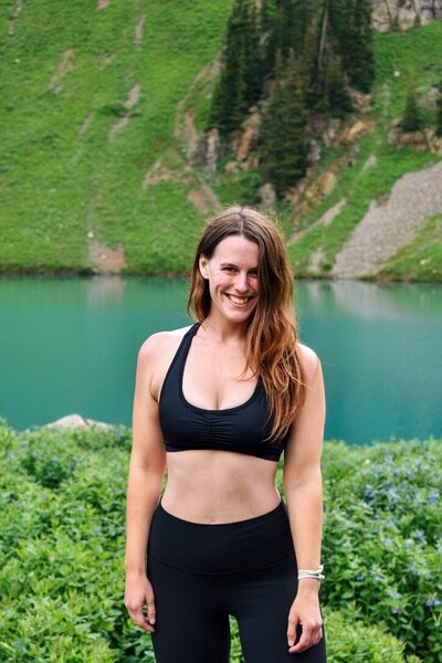 Woman wearing a black sports bra and leggings stands in front of Blue Lakes in Colorado.