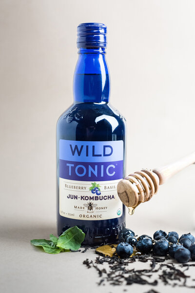 Blue bottle of Kombucha sitting in a pile of honey and blue berries