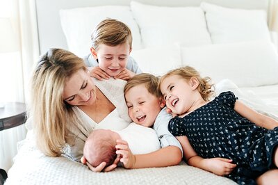 mother and four children laughing and snuggling on a bed