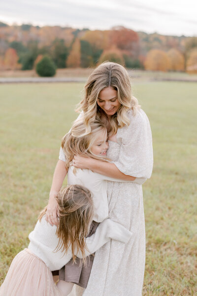 Mom hugging her daughters in a field. Image by Raleigh family photographer A.J. Dunlap Photography.