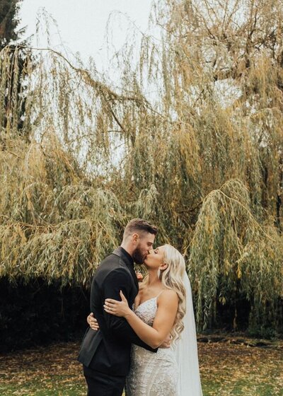 Bride and groom kissing under willow tree