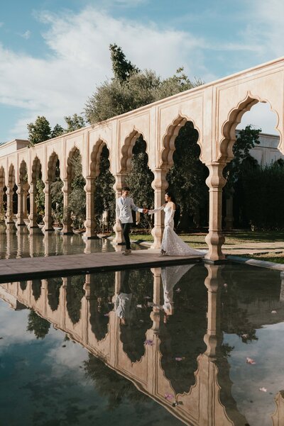 Moire and Tighe walking by the water holding hands after their wedding at Palais Namaskar Marrakech.