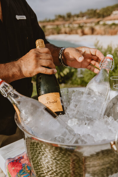 Hands place a bottle of Veuve Clicquot champagne and a glass bottle in an ice bucket, capturing a luxury event’s celebratory atmosphere with Socially Significant Events.