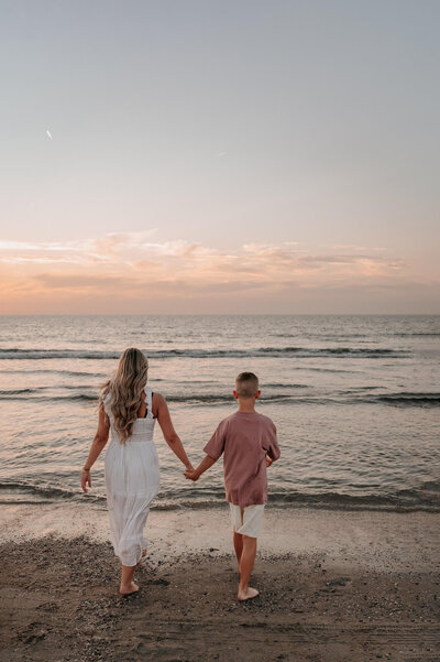 Mama en zoon lopen hand in hand naar het water op het strand