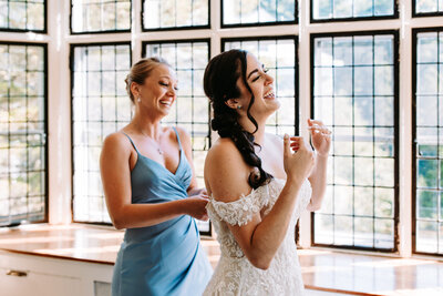 a photo of a mother helping her bride daughter into her dress on her wedding day in connecticut