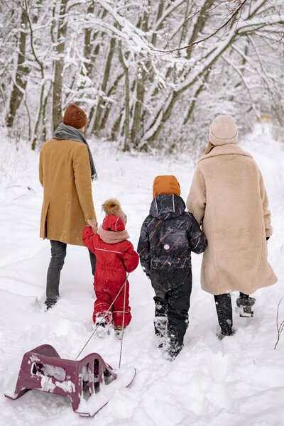 Two parents and two young children walk hand in hand through the snow, they are going sledding