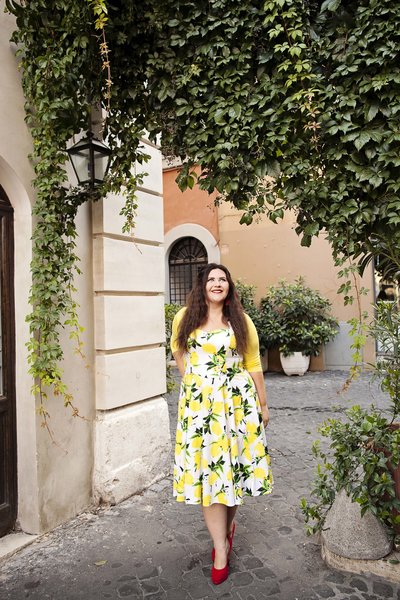 Girl in a yellow floral dress walking under Ivy. Taken by Rome Portrait Photographer, Tricia Anne Photography