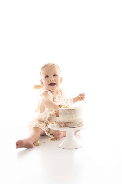 Baby smiling and grabbing cake for first birthday photo shoot.