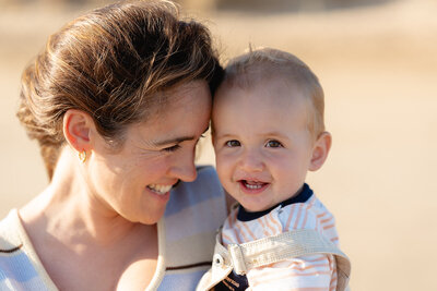 Close-up beach portrait in Geelong of a smiling mother holding her baby boy in warm afternoon light.