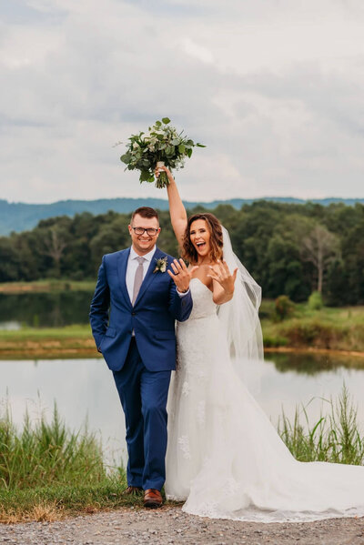 Photo of a bride and groom celebrating and showing off their new rings in front of a pond