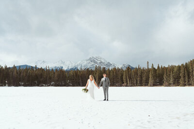Bride and groom holding hands in snowy landscape.