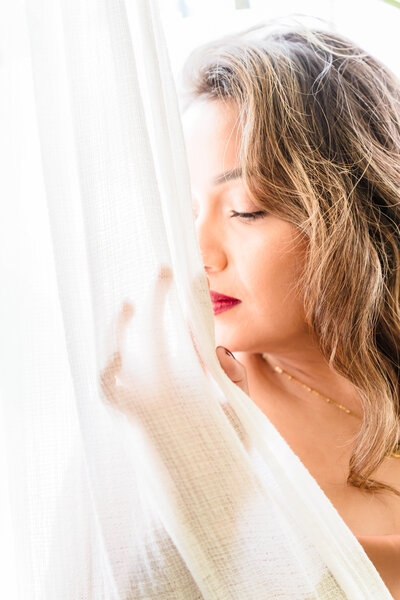 brand photo of a woman posing close to the sheer, eyes closed and looking out the window