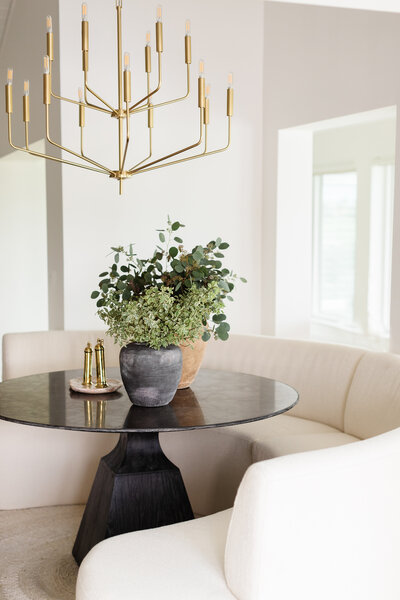 Neutral U-Shaped Couch, Paired Perfectly with a Sleek Black Circular Coffee Table, Gold Accents, Stone Pots, and Lush Greenery