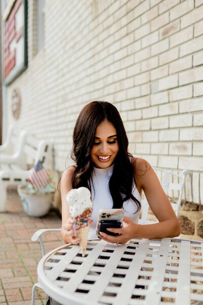 smiling woman holding an ice cream on one hand and a mobile phone on the other