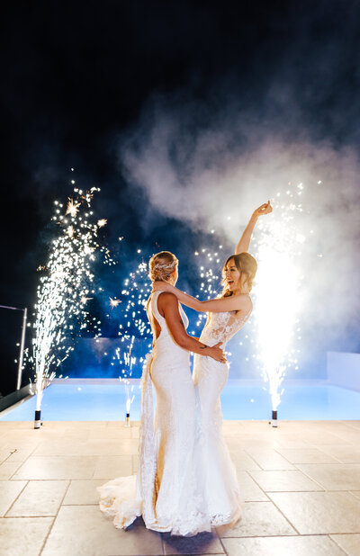 two brides dancing with fireworks behind