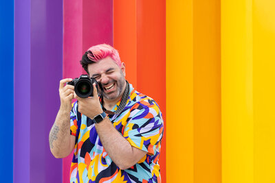 A photographer laughing as they hold their camera up to their eye.