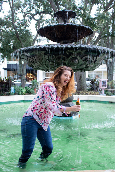 Woman standing  in a fountain holding a bottle of  champagne