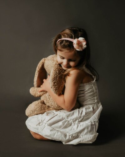 A little girl holding a teddy bear on a Pittsburgh-themed dark background in a heartwarming display of motherhood photography.
