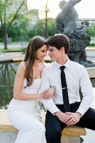 Wedding couple sitting at the edge of a fountain with their foreheads touching