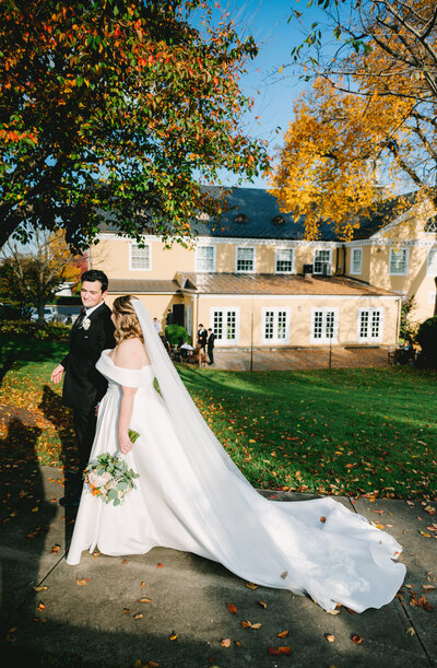 middleburg va wedding venue with bride and groom holding hands and walking across the lawn under orange and yellow trees at sunset