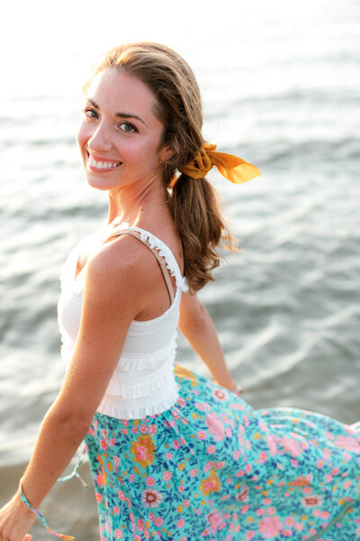 Best high school senior photographers. Colorful portrait of Nicole Marie Photography twirling in the wind. She is wearing a colorful floral maxi skirt and a yellow bow in her hair.