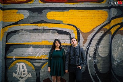 Engaged couple lean back against a colorful mural on a wall while holding hands during photo session