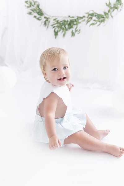 A toddler in a white and blue onesie sits in a studio
