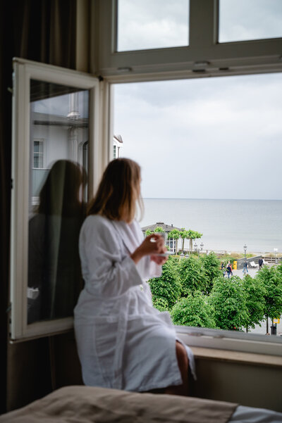 Frau trinkt Kaffee am Fenstereines Zimmers im LOEV Hotel und blickt auf das Meer.