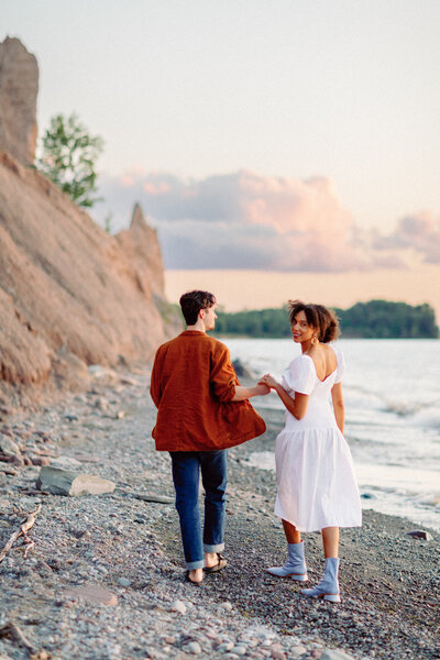Couple holding hands during their engagement session at Chimney Bluffs on Lake Ontario.