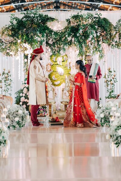 A couple dressed in traditional indian wedding attire participating in a ceremony with a celebrant.
