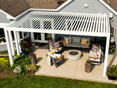 Aerial view of a white StruXure pergola with white louvers over a paver patio on the back of a house. 