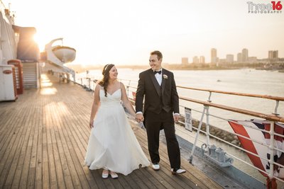 Bride and Groom walk hand in hand as they smile at each other on The Queen Mary in Long Beach