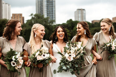 Bride and bridesmaids smiling at each other in front of Milwaukee skyline