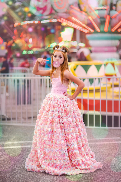 Redheaded girl with long hair wearing a rainbow dress and blowing a bubble gum bubble at a carnival near Annapolis Maryland