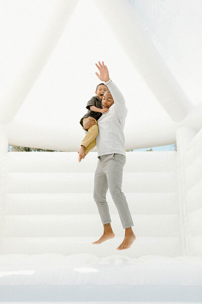 Father holding son bouncing in white bounce house