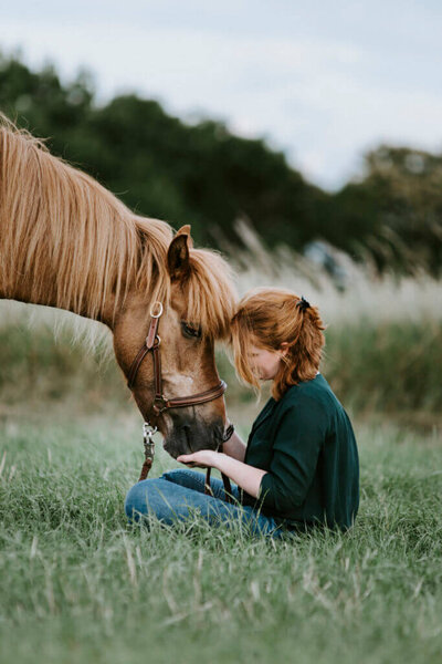 Eine Reiterin sitzt mit ihrem Islandpferd im Gras
