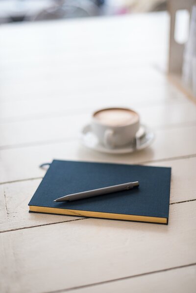 A cup of coffee beside a blue journal and a pen