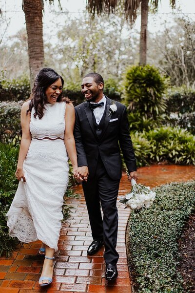 Bride and groom walk down a brick path laughing with each other