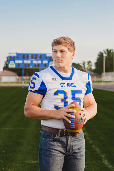 high school boy holding a football on his field