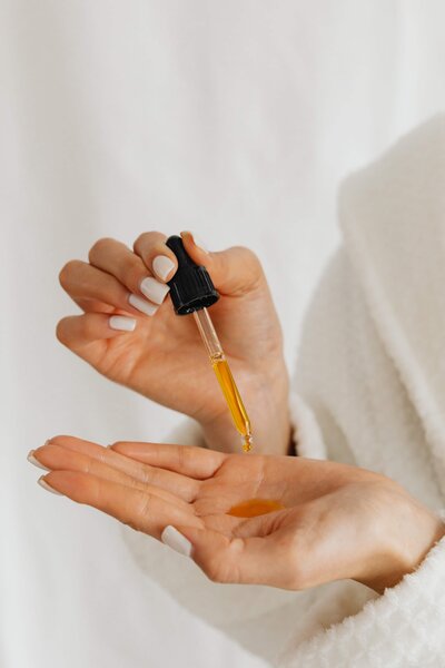 A woman dispensing a skincare serum with a dropped into her hand.
