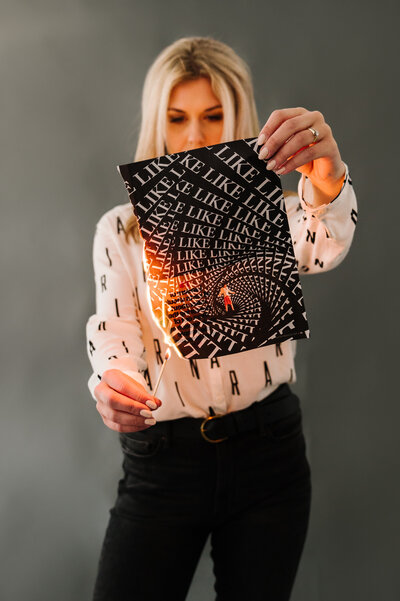 Sarah Klongerbo holding up a magazine page and lighting it on fire with a match