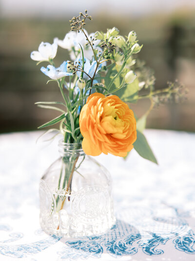 Orange ranunculus and light blue delphinium in pressed glass vase on blue and white tablecloth at Brasada Ranch