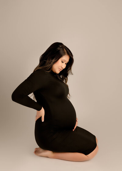 Mama holding bump looking down at baby bump in studio by Ashley Nicole Photography.