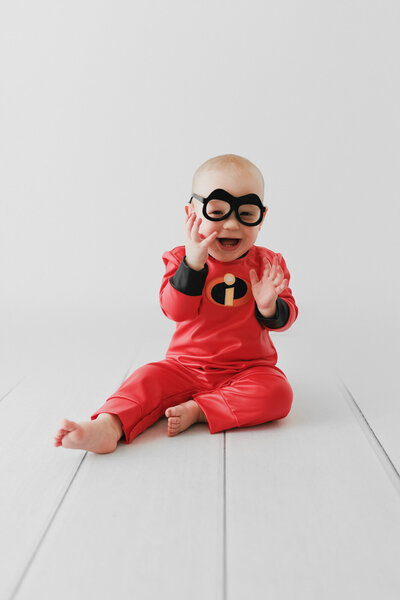 baby boy smiling wearing Incredibles outfit with glasses on his face