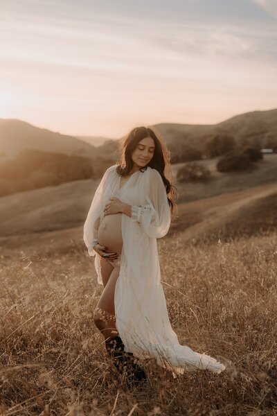 A pregnant woman standing in a field at sunset.