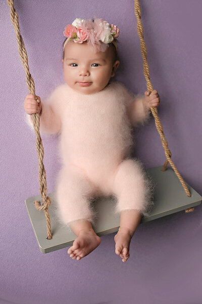 Awake newborn baby posing on swing and purple blanket  at her newborn session.