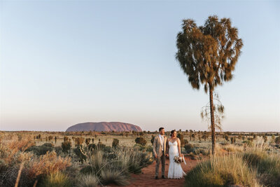 An Uluru wedding and elopement showing a bride and a groom standing in the desert with Uluru in the background