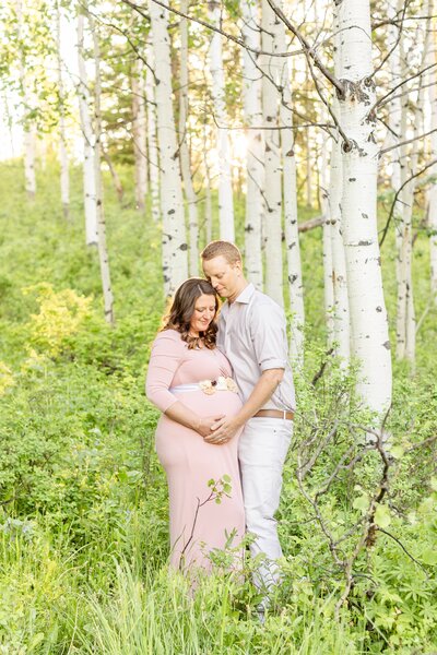 a pregnant woman embracing her husband amongst trees
